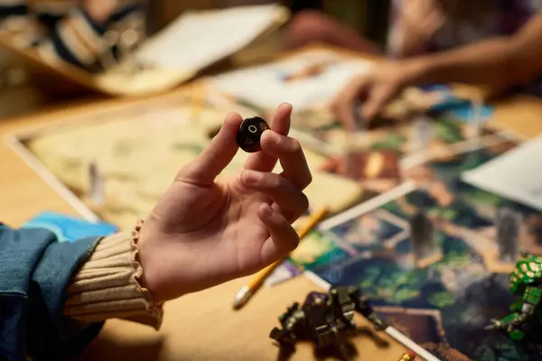 stock image Hand of unrecognizable youthful girl holding black dice in front of camera before throwing it on game board with character figurines