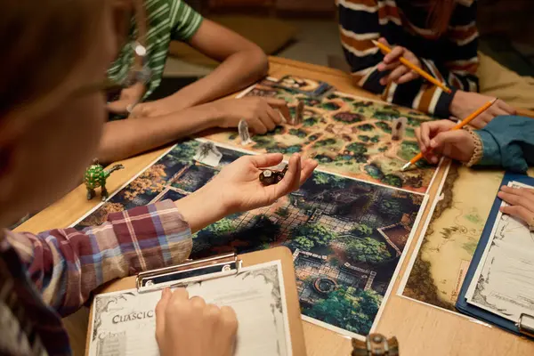 Oyun tahtasında, karakter figürleri ve masadan toplanmış bir grup kültürler arası genç oyuncuyla birlikte bir çocuk eli.