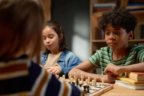 stock image Serious African American schoolboy in striped t-shirt thinking of next move and looking at chess board with pawns and other figurines