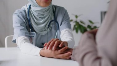 Klinikte oturan ve hamileliğinden endişe duyan, tanınmayan Afrikalı Amerikalı bir kadını sakinleştiren, İslami başörtüsü takmış, nazik, nazik, genç bir kadın jinekolog.