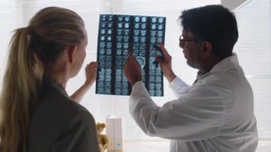 Yetişkin Hintli erkek nörologların orta boy görüntüsü. Kafkasyalı kadın hasta MRI taraması yapıyor. Beyin hasarından sonra anormallikleri gösteriyor.