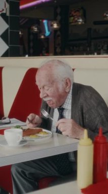 İleri yıllarda otantik Amerikan lokantasında kahvaltının tadını çıkaran beyaz bıyıklı adamın dikey yan görüntüsü.