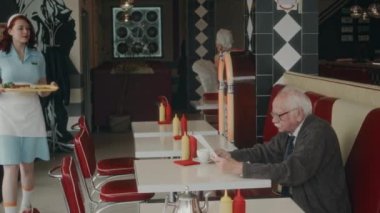 Kafkasyalı mavi üniformalı genç garsonun 1970 'lerde boş bir lokantada üst düzey erkek müşteriye kahvaltı servisi yapması.