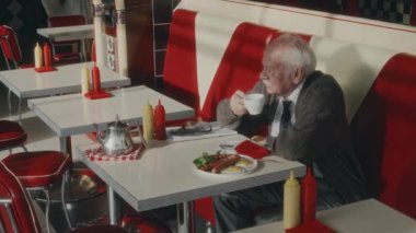 İlerlemiş yıllarda yakışıklı beyaz bir adamın sabah kahvesini yudumlarken 1980 'lerin tarzında bir lokantada kahvaltı ederken çekilmiş bir fotoğrafı.