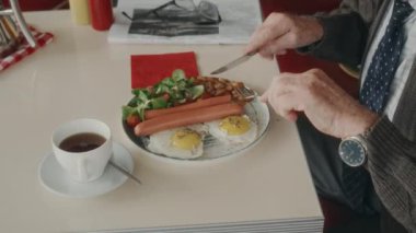 Sosisli yumurta ve fasulyeden oluşan klasik İngiliz kahvaltısı yapan tanınmamış üst düzey bir adamın yüksek açılı görüntüsü.