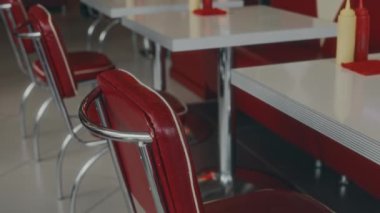 Kırmızı ve beyaz renklerde otantik bir restoranda, boş masaların yanındaki kırmızı deri koltuklardan çekilen insanlar yok.
