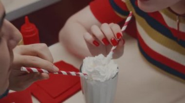 Kimliği belirsiz genç bir çiftin kafede romantik bir buluşmada aynı bardaktan kremayla milkshake yudumlarken yüksek açılı bir fotoğrafı.