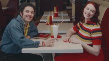 Milk shake ile poz veren ve otantik bir restoranda romantik bir randevuda el ele tutuşan mutlu beyaz bir çiftin yan portresi.