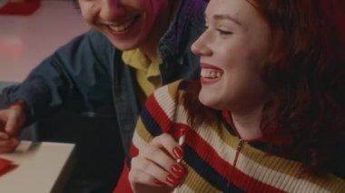 Kafkasyalı mutlu çiftin yakın planda gülüp eğlenirken neon ışıklı kafede milkshake içip, eğlenceli hikayeler anlatırlar.