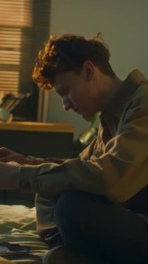 Depresyonda ve hayal kırıklığına uğramış genç bir adamın şafak vakti eski fotoğraflara bakarken dikey görüntüsü. Geçmişi düşünürken umutsuzluk hissetmek