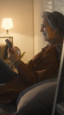 Kafkasyalı son sınıf öğrencisinin akıllı telefondan komik bir mesaj ya da hikaye okurken ve akşam yatakta yüksek sesle kahkaha atarken çekilmiş dikey yan görüntüleri.