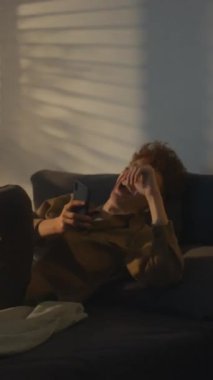 Yatakta kahkahalarla kahkahalarla kahkahalarla kahkaha atan genç bir adamın dikey yan görüntüsü. Telefonda komik videolar izlerken ya da internette arkadaşlarıyla sohbet ederken.