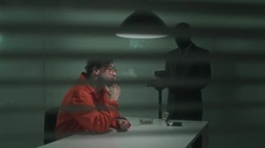 Tutukluları sorgulamaya hazırlanan çeşitli polis dedektiflerinin pencere perdelerinden vurularak, video kamera ve dava dosyaları kurarak masada otururken, turuncu takım elbiseli şüpheli sigara içerken,
