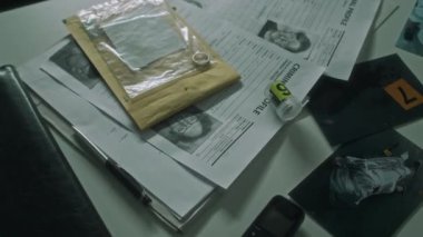 Yakın plan hiç kimse suç mahalli ilanlarından, numaralandırılmış olay yeri fotoğraflarından, telefondan, alyanslı zarftan plastik çantadan, gözlüklerden, silahtan, sorgu odasındaki masanın üzerine serilmemiş.