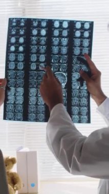 Hintli erkek nörolojistin hastaya MRI taraması yaparken, beyin hasarından sonra anormalliklere işaret ederken, hastanede danışmanlık yaparken dikey yakınlaştırma görüntüsü.