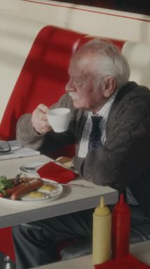 İlerlemiş yıllarda yakışıklı beyaz bir adamın 1980 'lerin tarzında kahvaltı yaparken sabah kahvesini yudumlarken dikey yan görüntüsü.