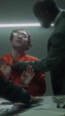 Sorgulama sırasında kızgın Afrikalı Amerikalı erkek federal ajanın sırıtan şüpheliyi boğazından yakalayıp salladığı, kadın ortağın onu durdurduğu, adamın gülüp dalga geçtiği orta boy dikey bir fotoğraf.
