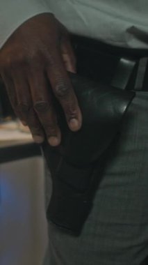 Kimliği belirsiz Afro-Amerikan erkek polis dedektifinin el tabancası kılıfına elini koyduğu dikey bir fotoğraf.