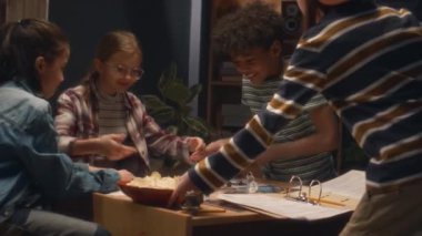 Akşamları evdeki masa oyununda çeşitli arkadaşlara patates cipsi ve patlamış mısır götüren beyaz çocuğun yan görüntüsü.