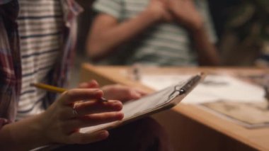 Kafkasyalı gözlüklü kızın oyun yöneticisi rolünde masa başı oyununun gidişatını düşünen ve akşam evde arkadaşlarıyla oynarken kağıtlara notlar alan yakın çekimi.