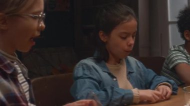 Çok ırklı çocukların masa oyunları kulübünde vakit geçirip patlamış mısır yerken domino oynarken çekilmiş el kamerası görüntüleri.