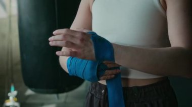 Genç ve zayıf Asyalı kadın boksörün yüz ve ellerinin orta boy yakın çekimi ya da mavi bandajlı elleri saran MMA dövüşçüsü, antrenmana ya da spor salonunda antrenmana hazırlanırken