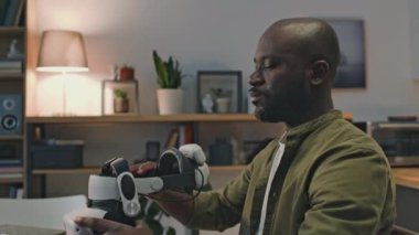 Siyah adamın günlük kıyafetlerini giyip, video gözlüğü takıp, internette çalışırken, evde el kol hareketleri yaparken yan yatmış görüntüsü.