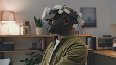 Siyah adamın VR gözlüklü göğüs üstü fotoğrafı. Arttırılmış gerçekliğe dalmış, evde çalışıyor.