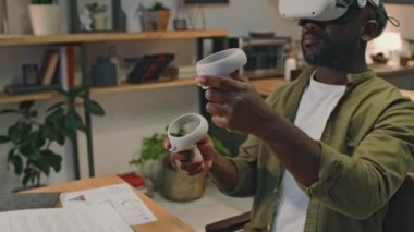 Siyahi iş adamının evden çalışırken kontrol cihazları ve artırılmış gerçeklik cihazları kullanarak modern teknolojiyi iş hayatında kullanmasının yan görüntüsü.