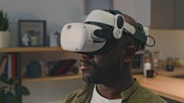 Siyah adamın VR gözlükleriyle büyümüş gerçekliği deneyimlediği ve evdeki metazele dalmış bir şekilde etrafa bakındığı yakın plan.