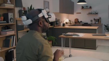 Sakallı bir adamın patlamış mısır yiyip film izlediği, gözlük taktığı ve evde yüksek teknoloji aletlerinin keyfini çıkardığı bir fotoğraf.