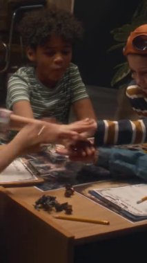 Bir grup çok ırklı çocuğun dikey çekimi akşam evde masa oyunu oynamak ve şans oyunu için el ele tutuşmak için toplandı.