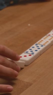 Kapalı bir masada oynarken domino taşlarını diziye yerleştiren isimsiz çocuğun elleri dikey yakın plan.