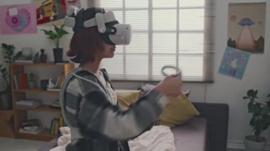 Arc shot 'ta kızıl saçlı genç kız arttırılmış gerçeklik cihazları kullanarak yatak odasında oynarken sanal rakibine yumruk atıyor.