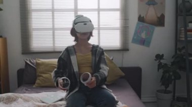 VR kulaklıklar ve yatak odasında sallanan kontrolörlerle oyun oynayan genç bir kız.
