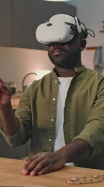 Yüksek teknoloji VR ekipmanlarıyla evden online çalışan Afrikalı Amerikalı işadamının dikey görüntüsü.