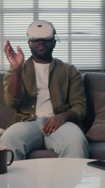 Oturma odasında kanepede otururken film seçen ve patlamış mısır alan siyah bir adamın dikey görüntüsü.