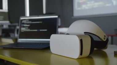 Bilgisayar sınıfında VR kulaklığı, bilgisayarın yanında, siyah arkaplanda yazılım kodlu, yenilikçi bilişim kursunda yakın plan çekilen kimse yok.