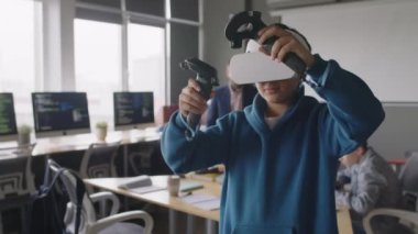 Sanal gerçeklik kulaklığı ve el bilgisayarı olan bir çocuğun orta ölçekli fotoğrafı. Projesini, programlama okulunda ders sırasında, boyutsal nesneleri manipüle ederek, teknolojiyle test ediyor.