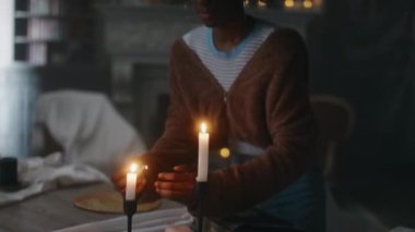 Afrika kökenli Amerikalı genç kız, rahat giysiler içinde karanlık ayinler yapmadan ve akşamları terk edilmiş evde kötü ruhları çağırmadan önce mum yakıyor.