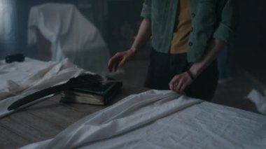 Kafkasyalı genç bir kızın esrarengiz bir kitap, büyük bir tüy ve çarşafla kaplı bir tahta bulurken, geceleri farklı arkadaşlarıyla birlikte terk edilmiş karanlık bir evi incelerken çekilmiş bir fotoğrafı.