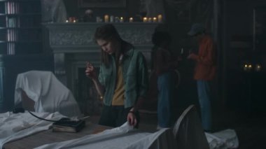 Kafkasyalı genç kız masada büyücülük aletleri buluyor ve karanlık boş köşkü gözlemlerken her şeye burnunu sokan arkadaşlarına gösteriyor.