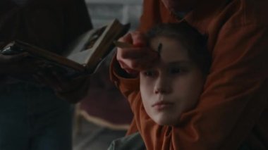 Arkadaşı okült kitaptan dualar okurken, şeytan çıkarma seremonisi yaparken, Palo Santo ahşap közle siyah haç çizen, kıvranan şeytani kızın alnına yapışmış bir adamın yakın çekimi.