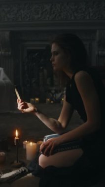 Solgun cadının yanan palo santo dualarını okurken dikey çekimi karanlık evde mum ışığında karanlık ayinler yapmadan önce yapıştı.