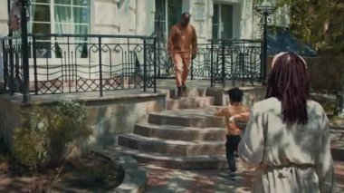 Genç Afro-Amerikan erkek ve kadının genç oğlu ziyarette akrabalarına yürürken, mutlu siyah amca ya da büyükbaba sundurmada yeğenine ya da torununa sarılırken tam bir fotoğrafı.