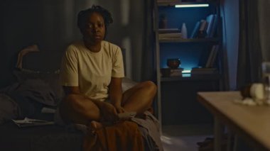 Şiş gözlü, şiş gözlü, bacak bacak üstüne atmış, kameraya bakan, travma sonrası uykusuzluk çeken yorgun Afrikalı Amerikalı kadının tam portresi.