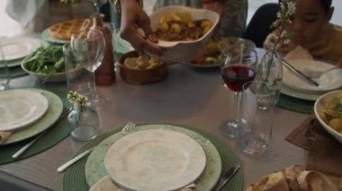 Uzun elbiseli, örgülü saçlı, orta boy Afro-Amerikalı bir kadın ve kocası masaya sıcak yemek koyarken, aile kahvaltısına hazırlanırken, bardakları ve tabakları düzenlerken.