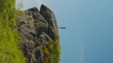 Dikey geniş açı, kaygısız turistin yavaş çekimleri güzel yaz manzarası altında tepede duruyor ve gökyüzüne zıplıyor.