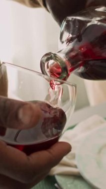 Ev kutlamaları sırasında ya da misafirlerle akşam yemeği yerken kırmızı şarap ya da dut şarabı bardaktan cama döken tanınmayan koyu tenli adamın dikey yakın çekimi.