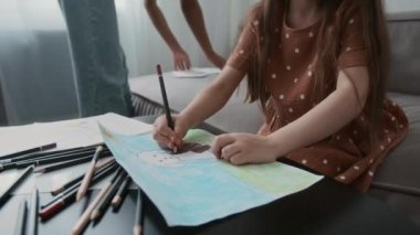 Orta boy beyaz bir kız, renkli kalemlerle resim çizerken Afro-Amerikalı genç bebek bakıcısıyla evde kalıyor.